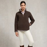 Woman wears brown fleece sweater over a pinstripe shirt and cream skinny jeans over a grey background